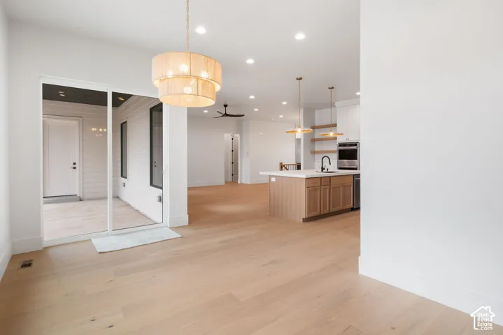 Open-concept area featuring light-tone wood-finish flooring, recessed lighting, a kitchen island with stone-surface countertops, tiered drum pendant lighting, and a large sliding glass door