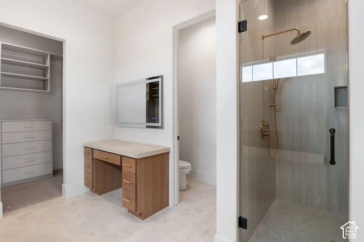 Walk-in shower with floor-to-ceiling tile, gold-finish fixtures, and a frameless glass door, alongside a built-in wood-finish vanity with stone countertop and integrated lighted mirror