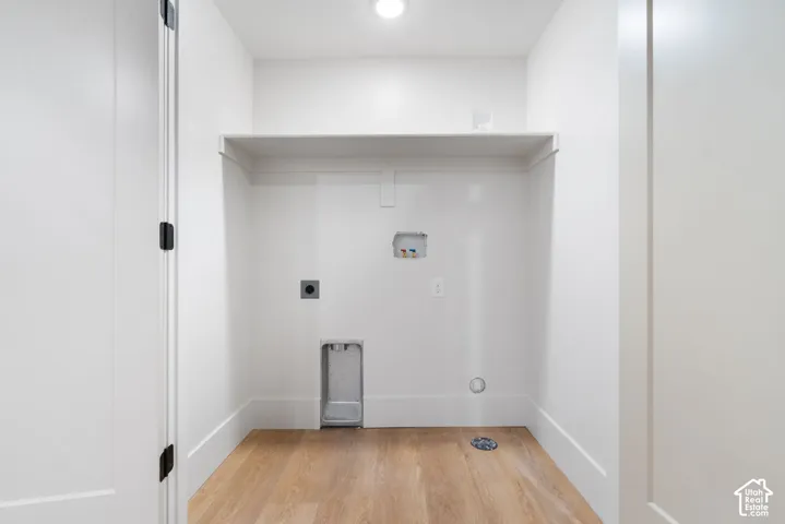Utility area featuring wood-finish flooring, recessed wall connections, and an overhead built-in shelf