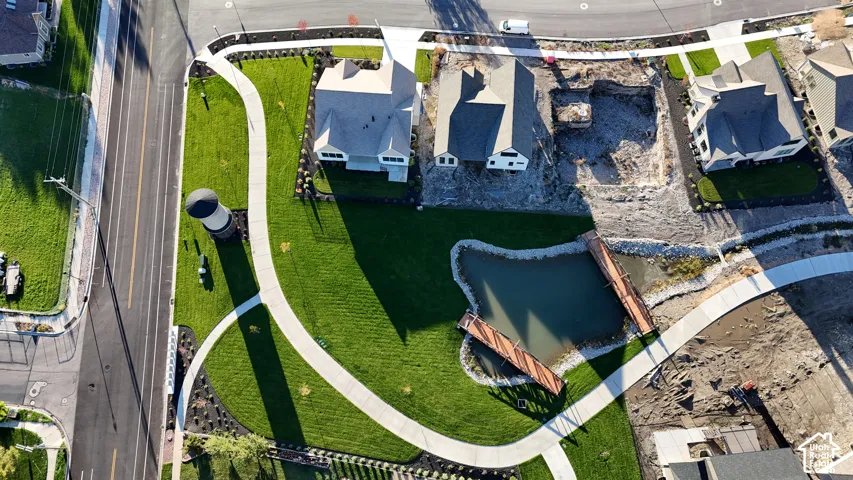 Aerial view featuring a pond, pedestrian bridge, expansive manicured lawn, and concrete walkways