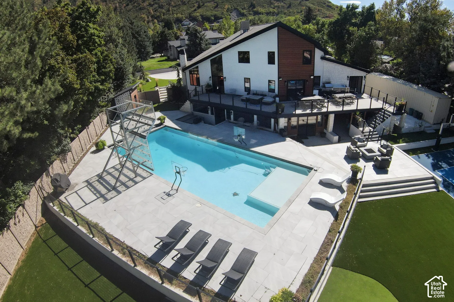 Exterior featuring a multi-level deck, swimming pool with built-in lounge area, stone patio, artificial turf lawn, and hillside backdrop