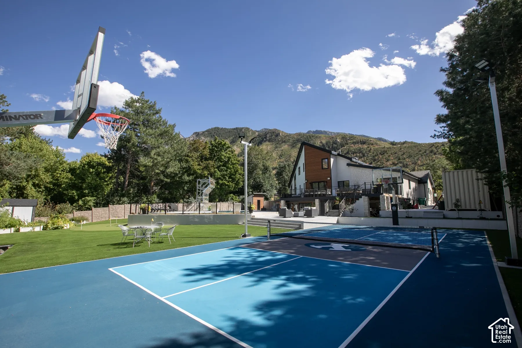 Outdoor recreational area featuring a multi-sport court with blue and gray surfacing, a built-in basketball hoop, a manicured lawn, and mountain scenery