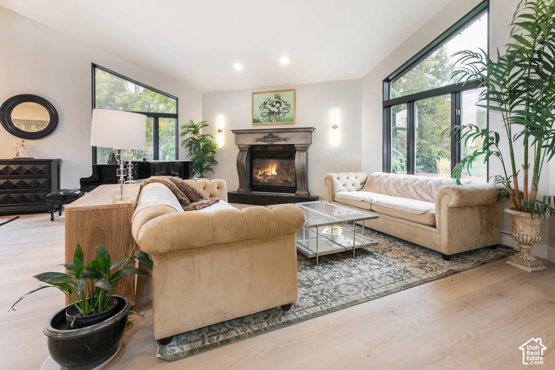 Living area featuring a vaulted ceiling, large picture windows with black frames, wood-finish flooring, and a decorative fireplace with a mantel