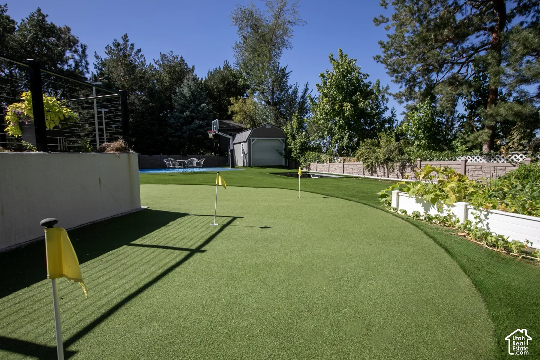 Backyard putting green with synthetic turf, raised planter boxes, detached storage shed, basketball hoop, and perimeter privacy fencing
