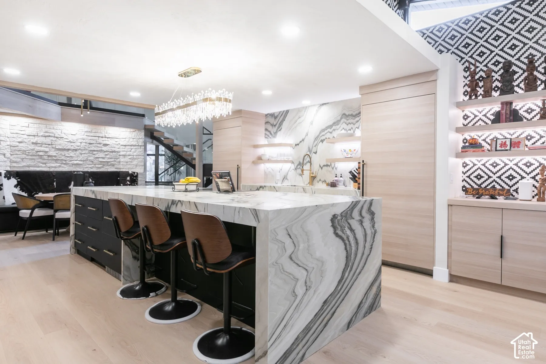 Kitchen island with waterfall stone countertop, integrated cabinetry, wood-finish flooring, textured stone accent wall, and geometric tile backsplash