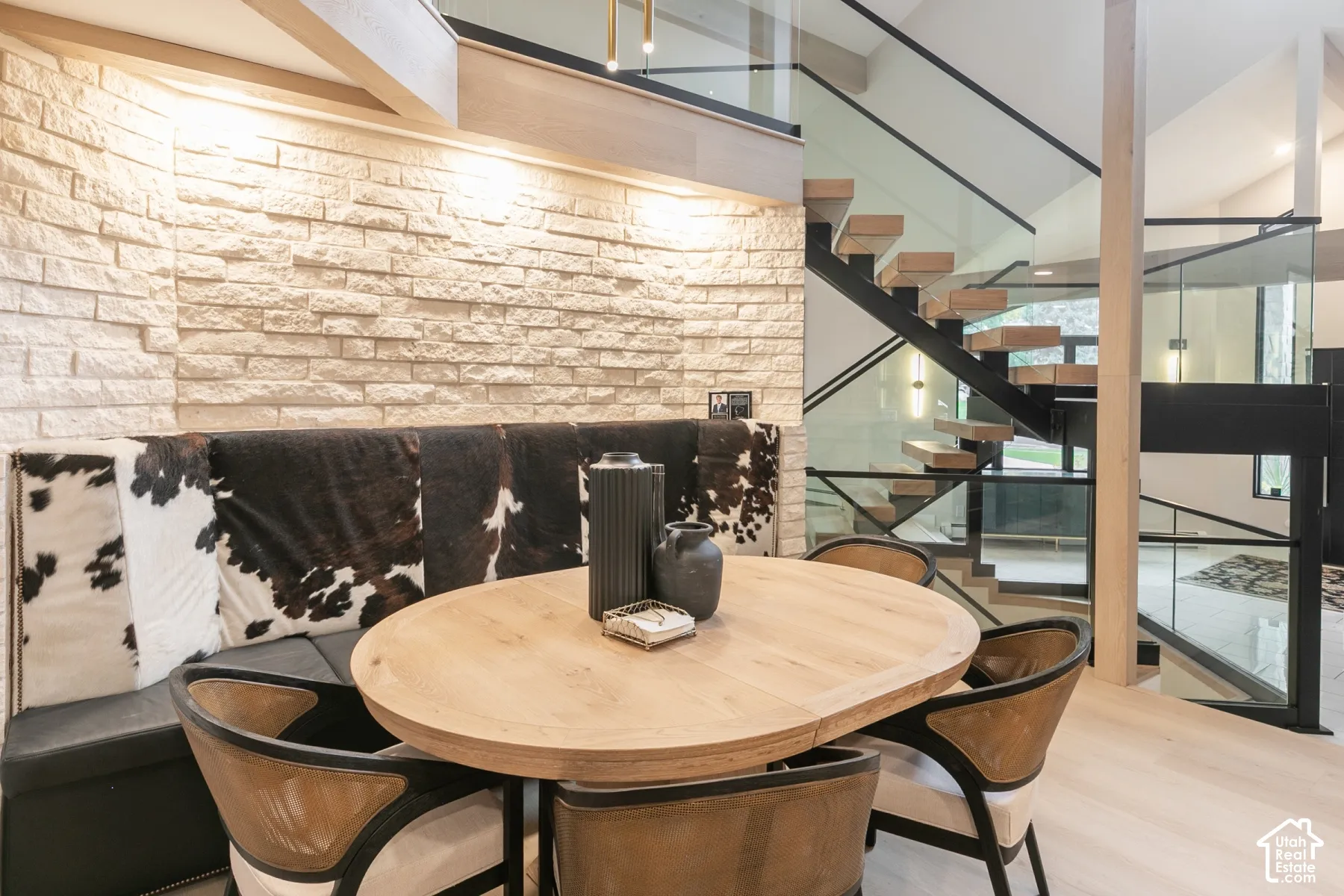 Textured stone accent wall, floating staircase with wood treads, black metal railing, glass balustrades, and wood-finish flooring