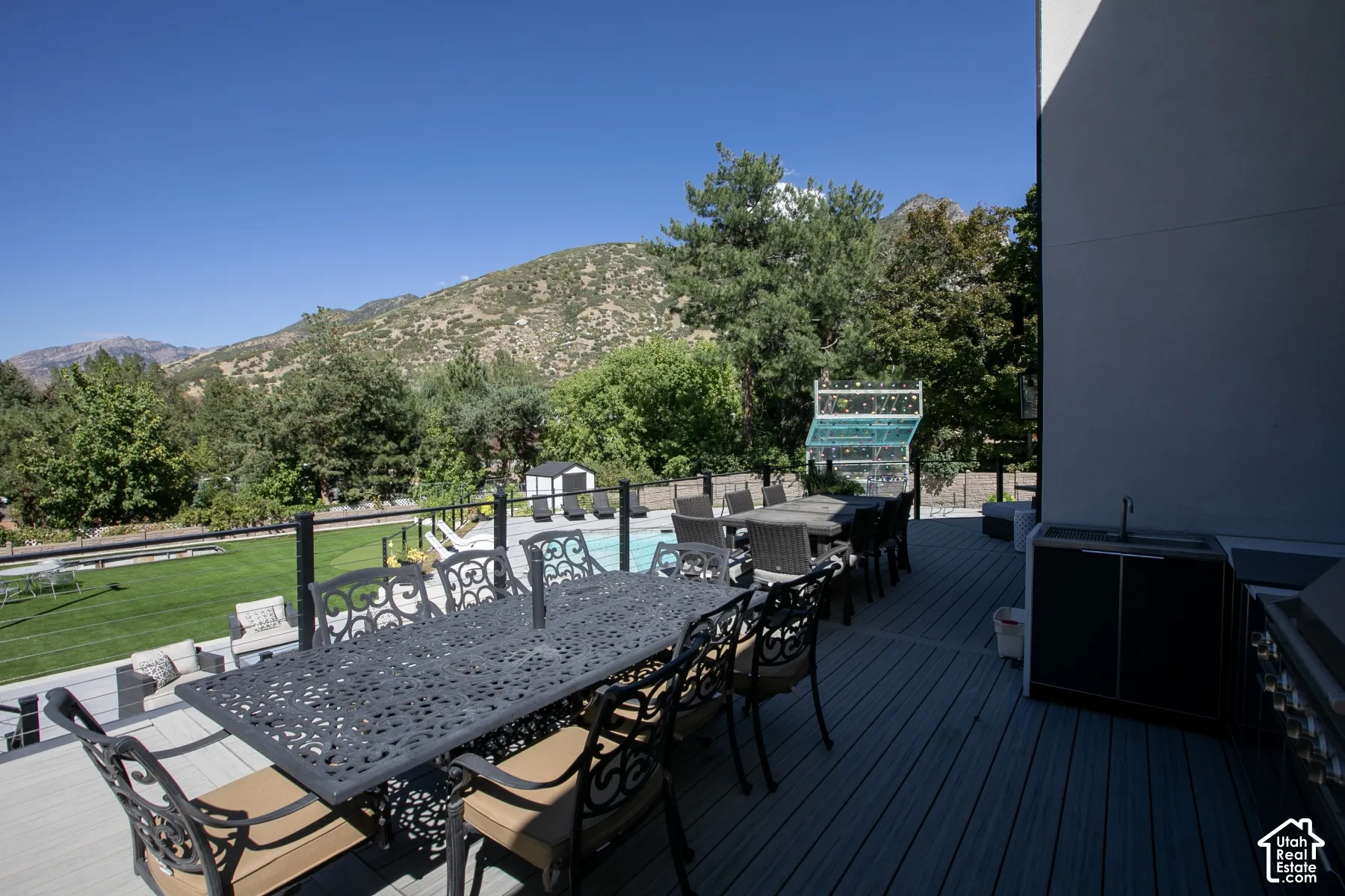 Elevated composite deck featuring a built-in outdoor kitchen, black metal railing, swimming pool, and mountain backdrop