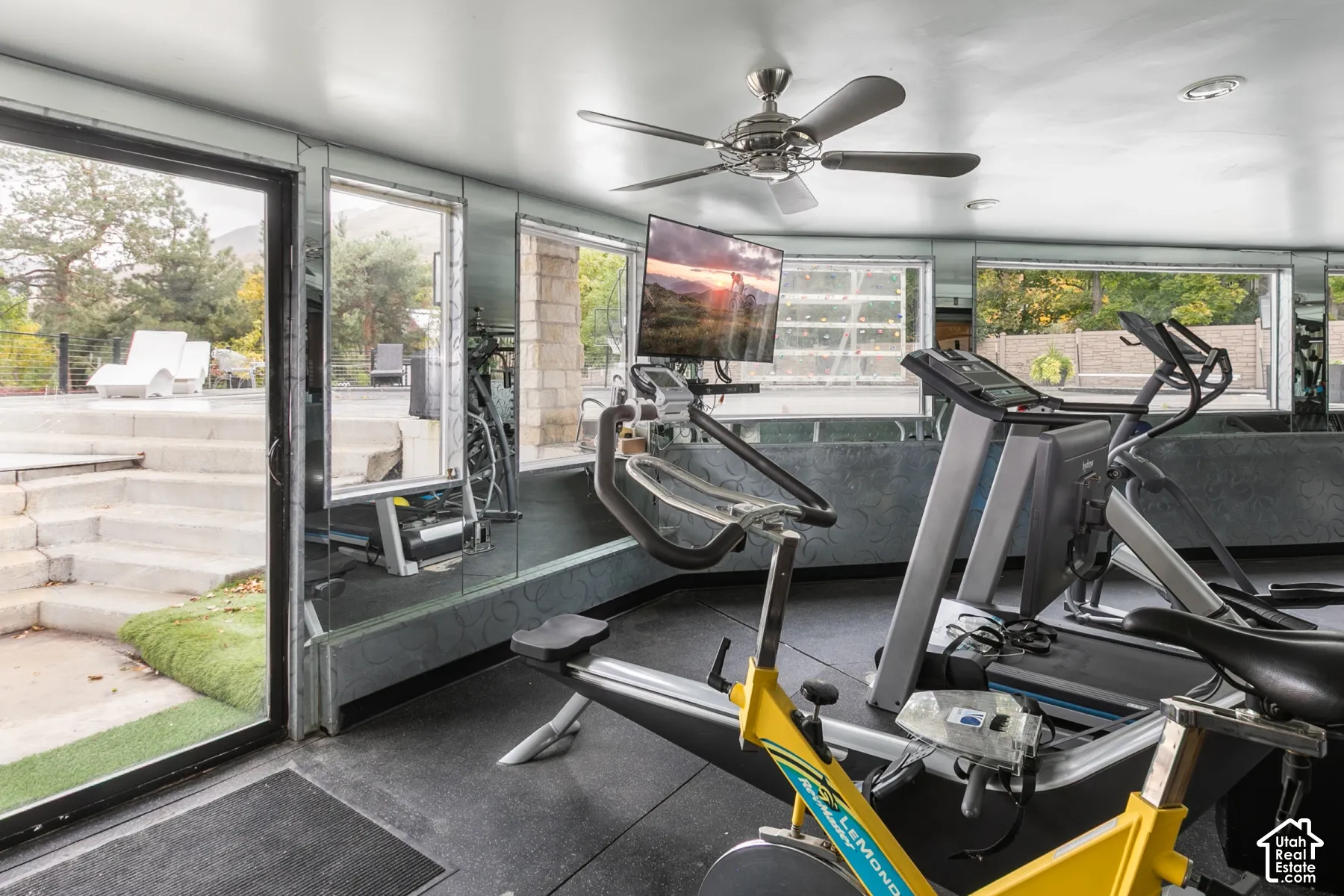 Floor-to-ceiling mirrored walls, multiple expansive glass windows, integrated ceiling fan, and direct exterior access via sliding glass door