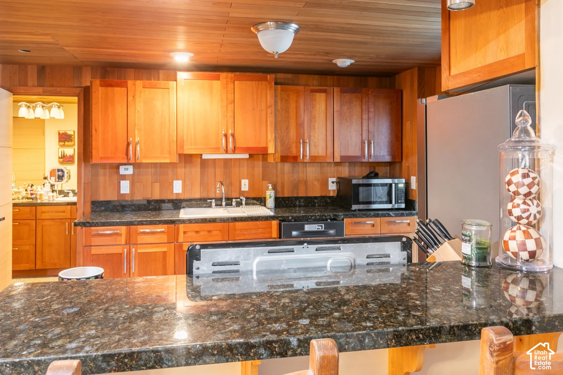 Kitchen featuring wood cabinetry, dark stone countertops, wood-paneled walls and ceiling, and an integrated bar-height counter
