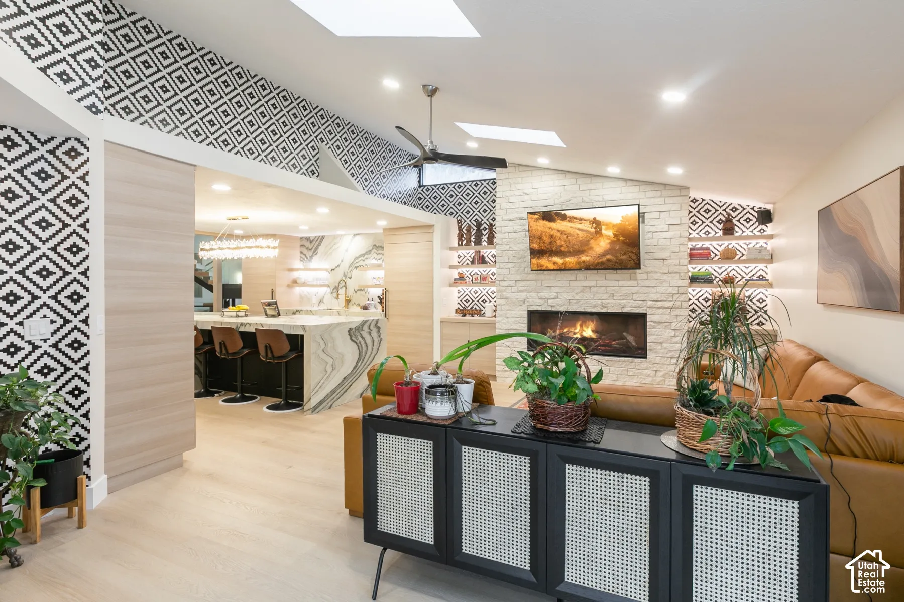 Vaulted ceilings with integrated skylights, floor-to-ceiling stone fireplace, recessed lighting, wood-finish flooring, and built-in shelving with pattern-tiled accent walls