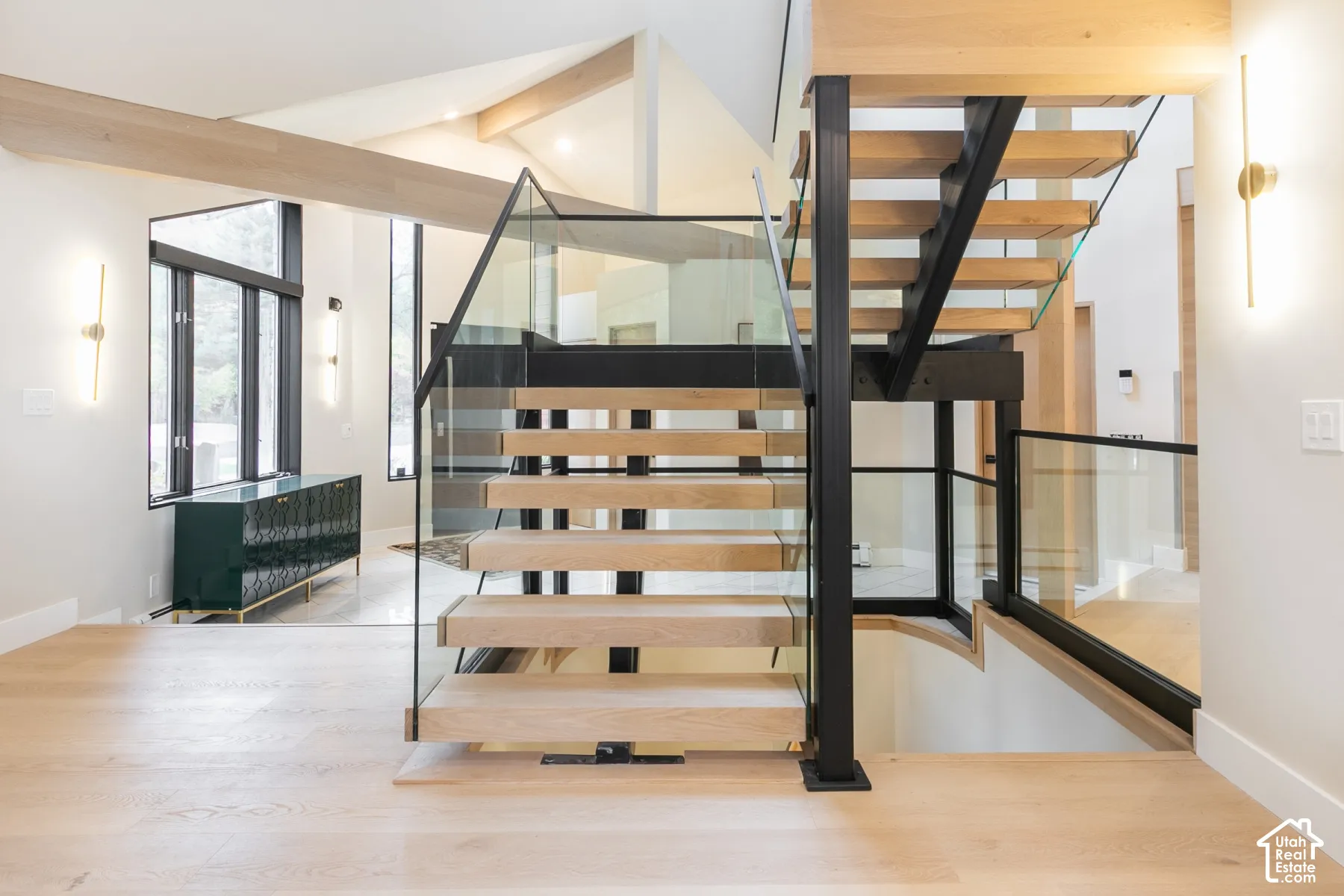 Open-tread staircase featuring wood-finish steps, a black metal frame, and glass panel railing