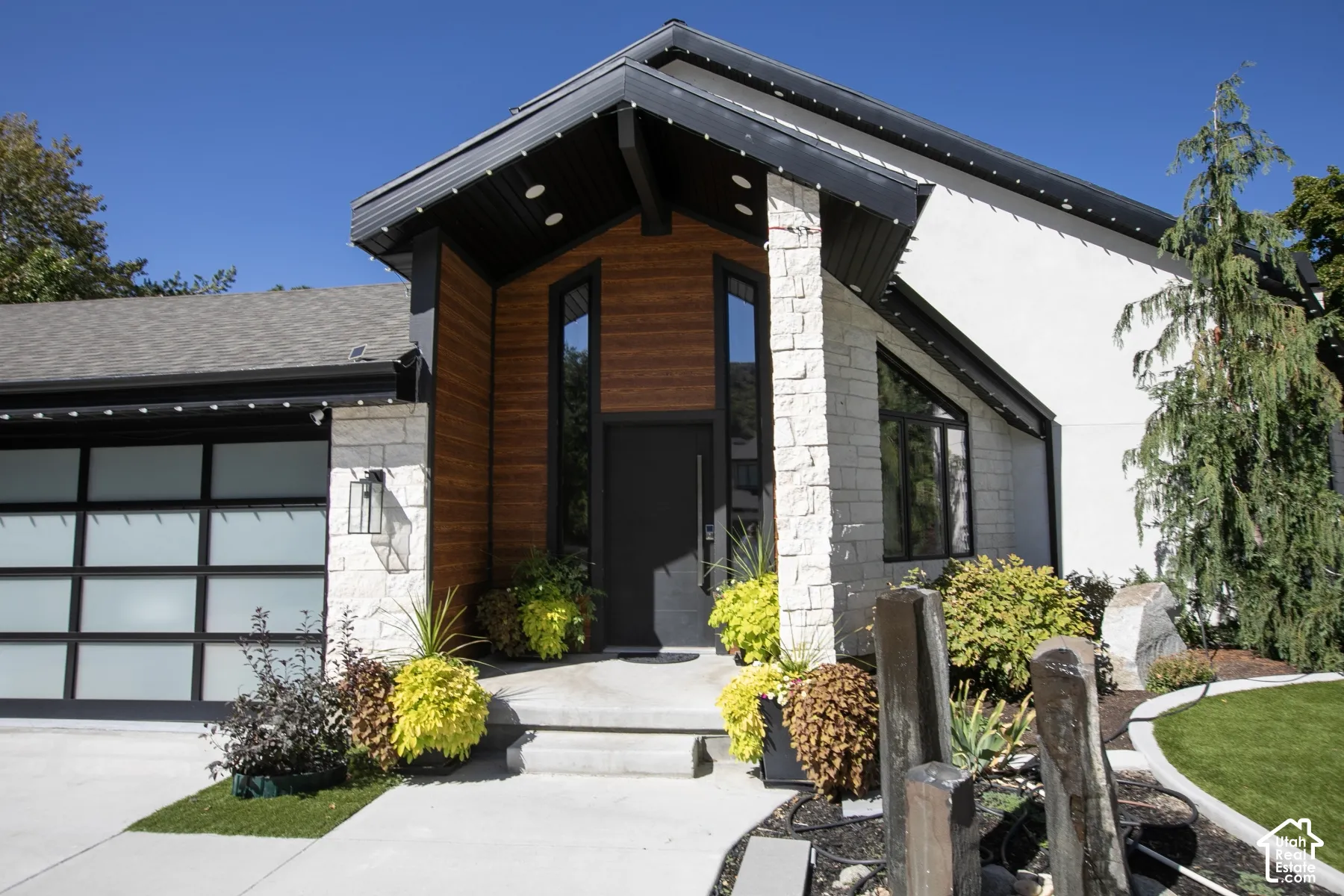 Modern exterior featuring stacked stone masonry, horizontal wood-finish siding, a frosted glass panel garage door, steep gable roofline, and vertical accent windows