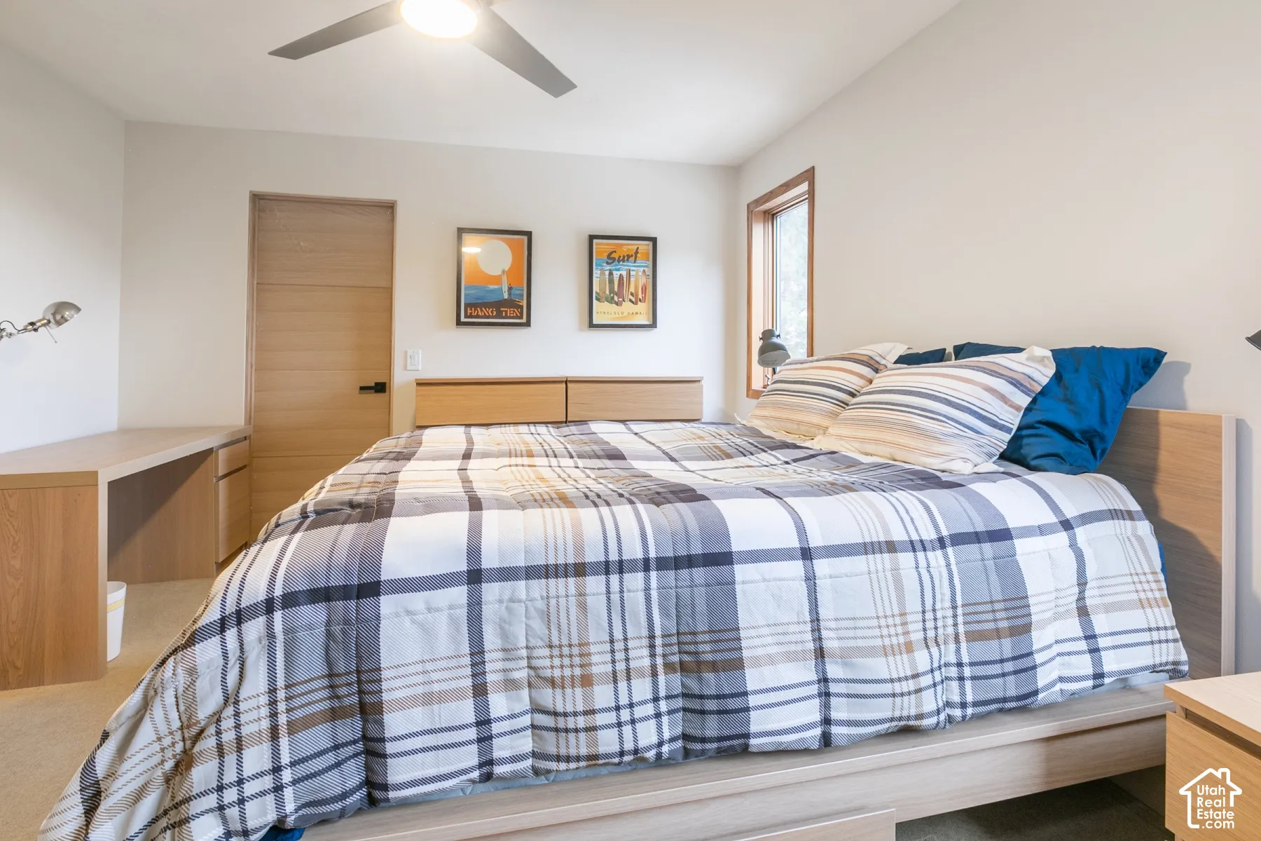 Neutral interior featuring horizontal wood-grain door, integrated wood-finish desk with storage, ceiling fan, and carpeted flooring