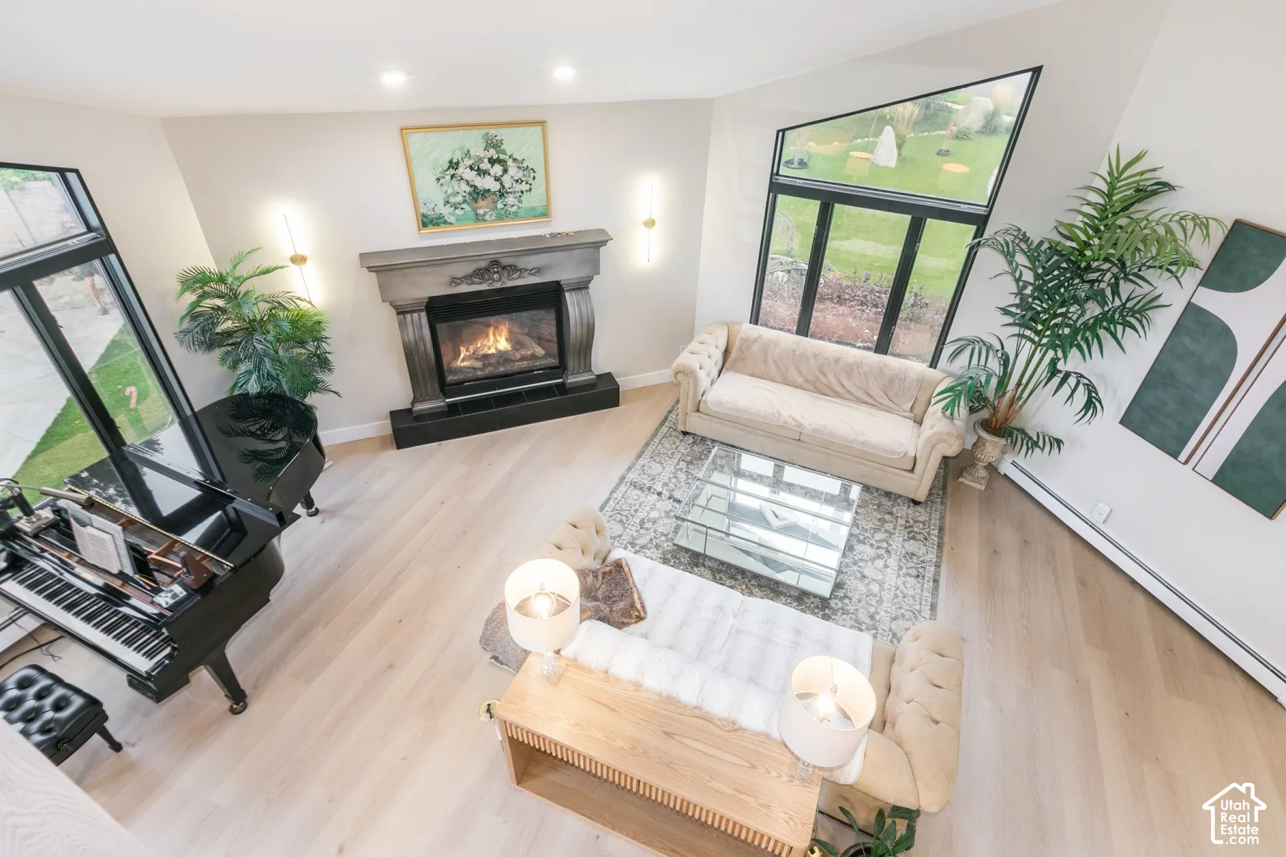 Living area featuring wood-finish flooring, vaulted ceilings, expansive floor-to-ceiling windows with black frames, and a prominent fireplace with a detailed mantel