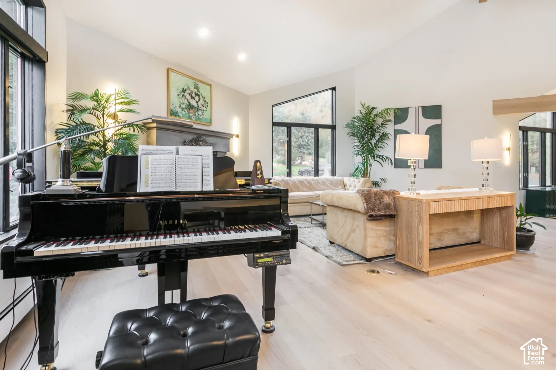 Vaulted ceilings with recessed lighting, light wood-finish flooring, floor-to-ceiling multi-pane windows, and a prominent fireplace with a stone mantel
