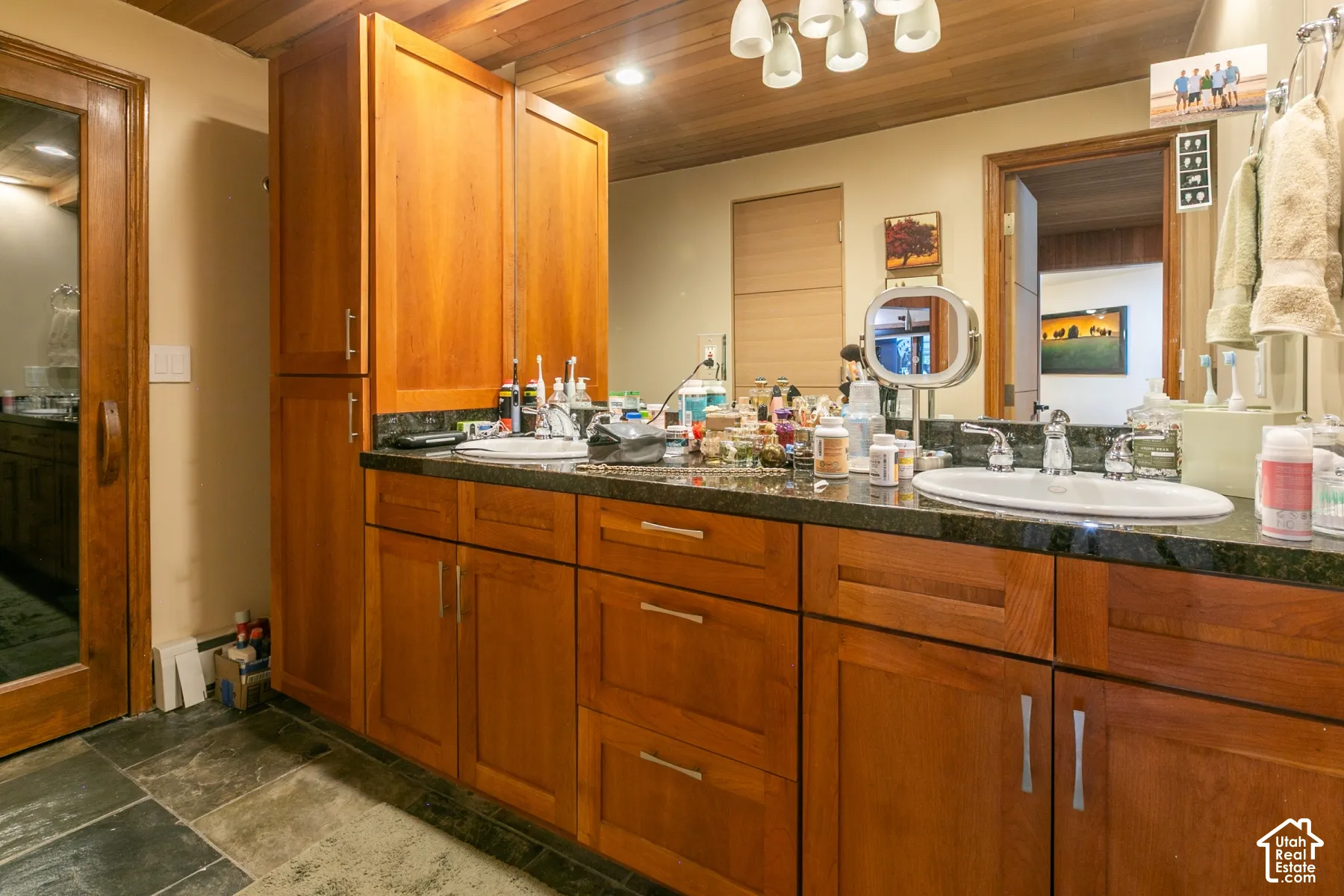 Dual-sink vanity with wood cabinetry, stone countertops, integrated cabinetry tower, and tongue-and-groove wood-plank ceiling