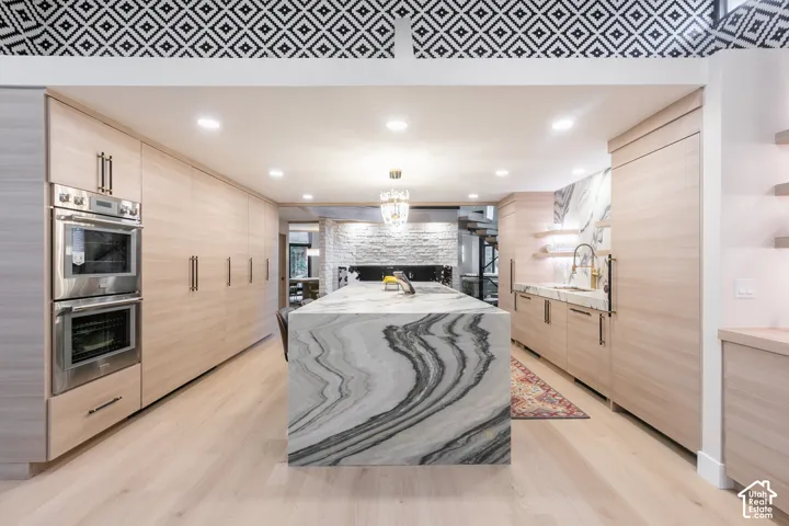 Kitchen featuring flat-panel wood cabinetry, a waterfall island with stone countertop, stainless steel double wall ovens, recessed lighting, and decorative patterned wallpaper