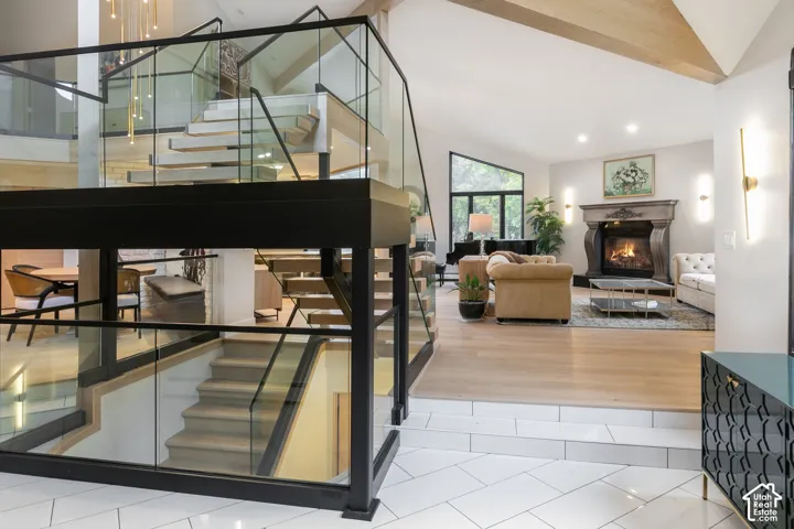 Staircase featuring floating wood treads, glass panel railings, and black metal framework, complemented by wood-finish flooring, white tiled surfaces, and a decorative fireplace mantel