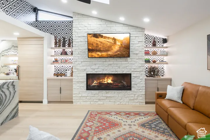 Stacked stone fireplace with a linear firebox, light wood-finish cabinetry, built-in shelving, patterned accent wall, and recessed ceiling lighting
