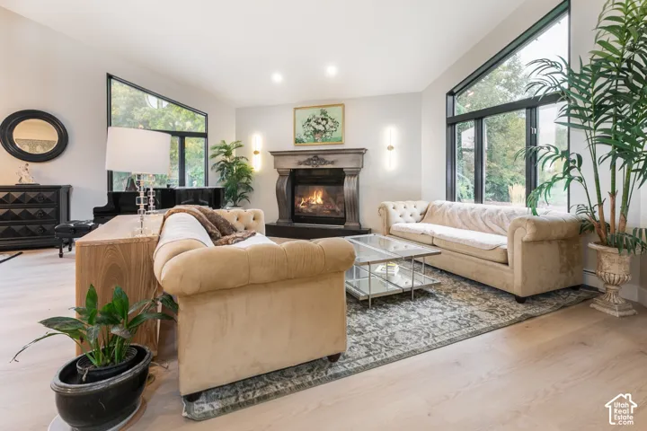 Living area featuring a vaulted ceiling, large picture windows with black frames, wood-finish flooring, and a decorative fireplace with a mantel