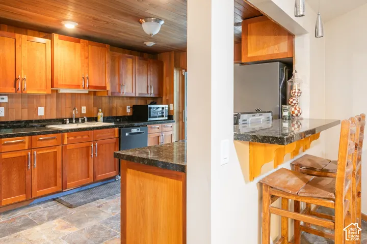 Kitchen featuring custom wood cabinetry, dark stone countertops, natural wood-paneled ceiling, and stone tile flooring