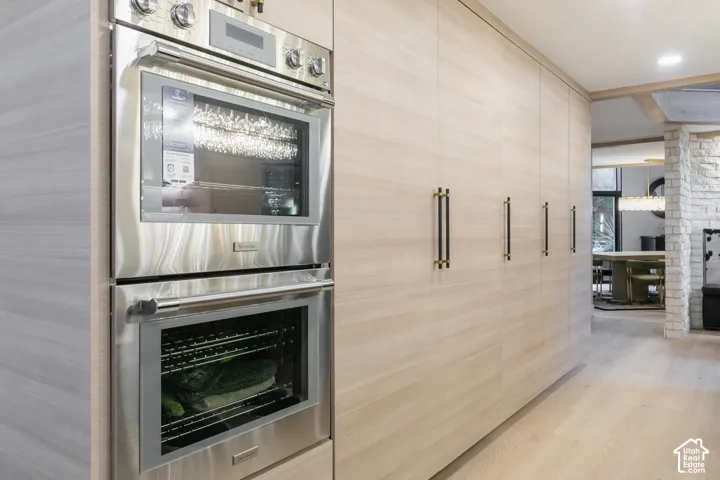 Built-in stainless steel double wall ovens, floor-to-ceiling flat-panel cabinetry with linear hardware, wood-finish flooring, and exposed light-colored stone column