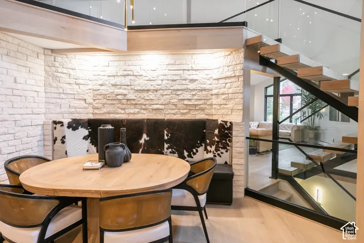 Textured white stone accent wall, floating wood-tread staircase with black metal framing, glass panel railing, and light-tone wood-finish flooring