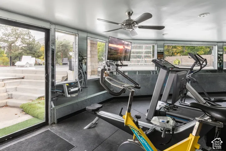 Floor-to-ceiling mirrored walls, multiple expansive glass windows, integrated ceiling fan, and direct exterior access via sliding glass door