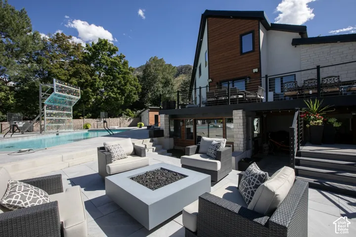 Multi-level patio featuring a built-in fire pit, stone-tile hardscaping, in-ground pool, and tiered wood-finish and metal balcony railing