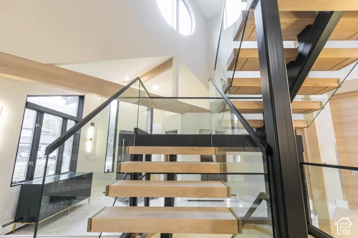 Floating staircase featuring wood treads, black steel supports, and glass railings, accented by high ceilings with circular windows and natural wood beams