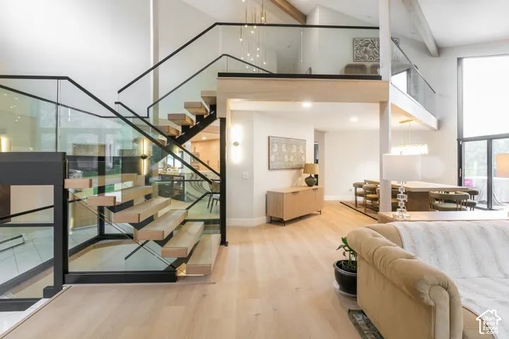 Open-riser staircase with wood treads and glass railings, wood-finish flooring, vaulted ceilings with exposed beams, and floor-to-ceiling windows