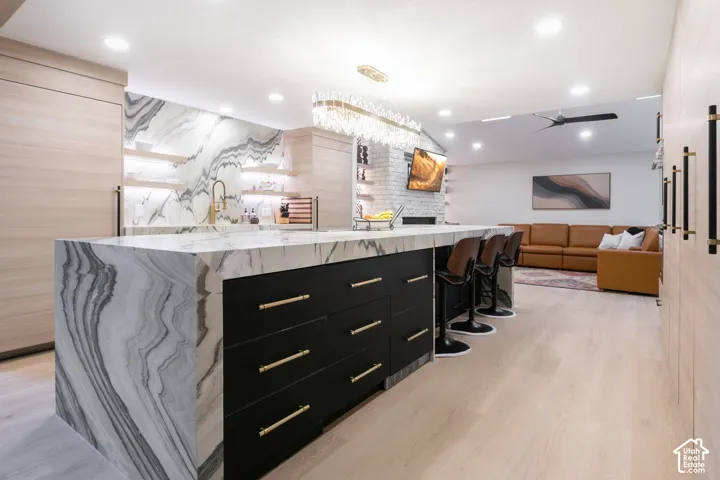 Kitchen featuring a waterfall-edge island with stone surfacing, matte black cabinetry with gold-tone hardware, wood-finish cabinetry, recessed lighting, and a crystal chandelier
