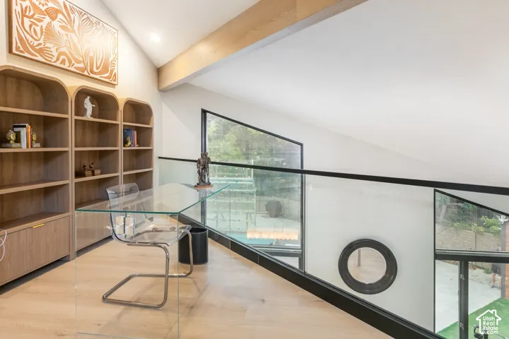 Vaulted ceiling featuring an exposed wood beam, floor-to-ceiling built-in arched cabinetry, wood-finish flooring, and a glass partition with a matte black railing