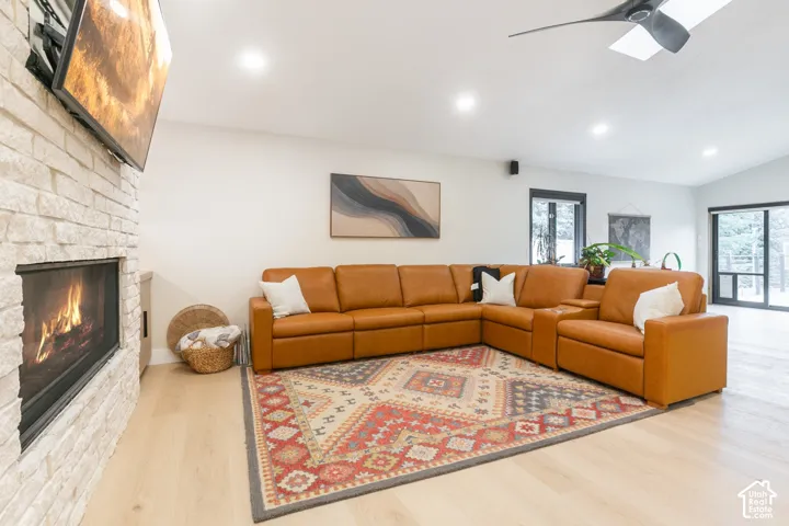 Light-toned wood-finish flooring, floor-to-ceiling stone-veneer fireplace, vaulted ceiling, recessed lighting, and matte black ceiling fan