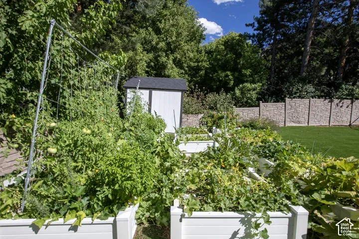 Backyard featuring raised garden beds, a storage shed, a manicured lawn, and stone-textured privacy fencing