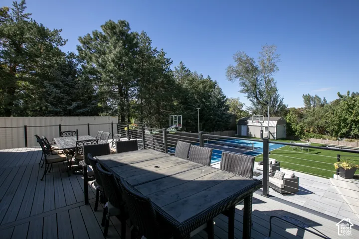 Elevated composite deck featuring horizontal cable railing, multi-use sports court, artificial turf lawn, and detached storage structure