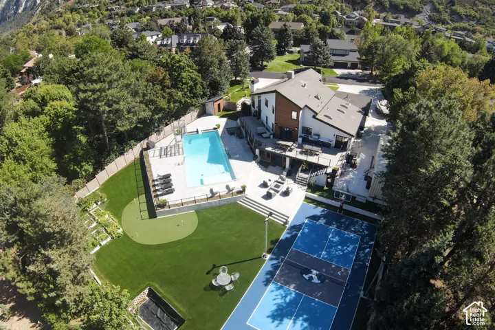 Aerial view featuring an in-ground swimming pool with stone surround, a multi-use sports court, a putting green, and a multi-level deck