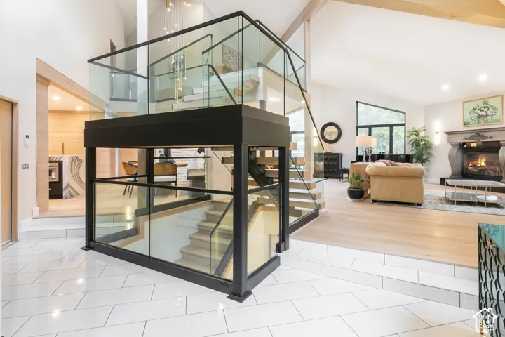 Floating staircase featuring a matte black metal frame and glass railings, polished light-toned tile flooring in a herringbone pattern, wood-finish flooring on the upper level, and a stone fireplace surround