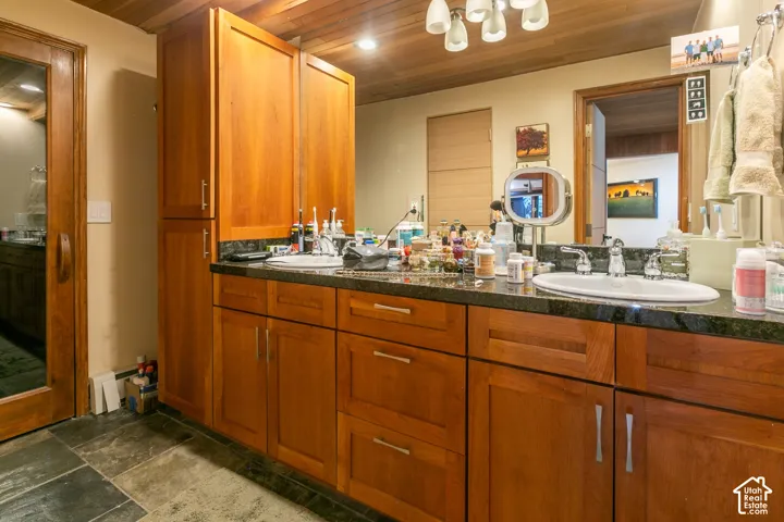 Dual-sink vanity with wood cabinetry, stone countertops, integrated cabinetry tower, and tongue-and-groove wood-plank ceiling