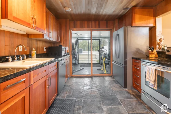 Kitchen featuring natural wood paneling, wood-plank ceiling, stone-finish flooring, dark stone countertops, and stainless steel appliances