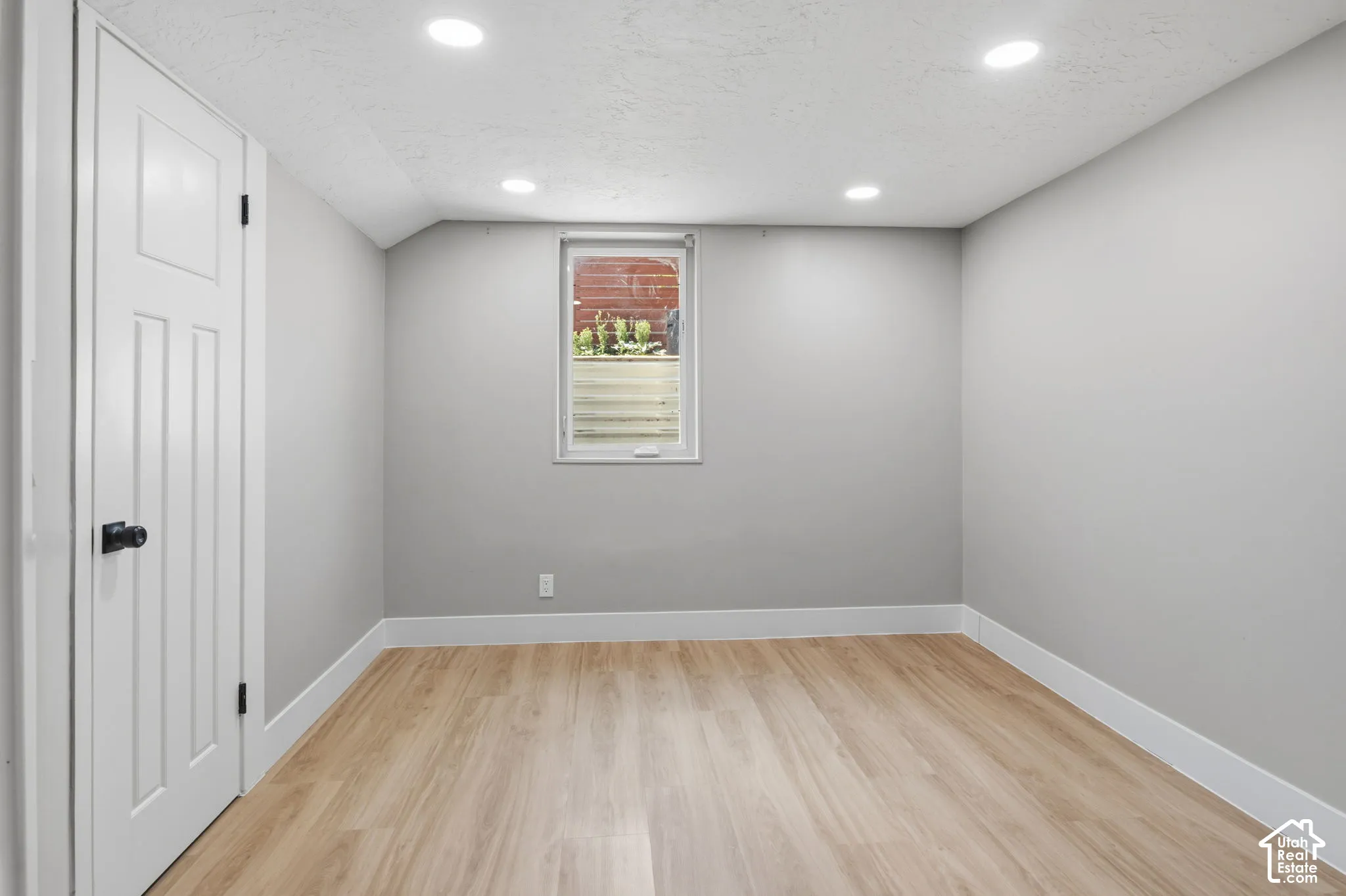 Room featuring neutral paint, recessed lighting, wood-finish flooring, and a single-hung window with a window well