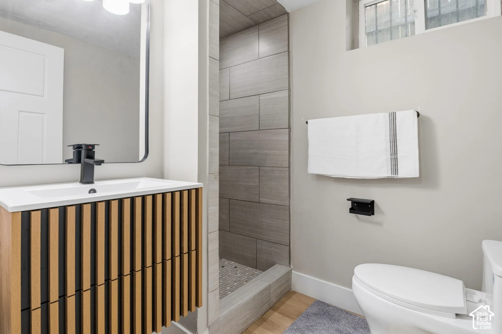 Bathroom featuring a wood-slat vanity, rectangular vessel sink with matte black faucet, and a walk-in shower with horizontal grey tile surround