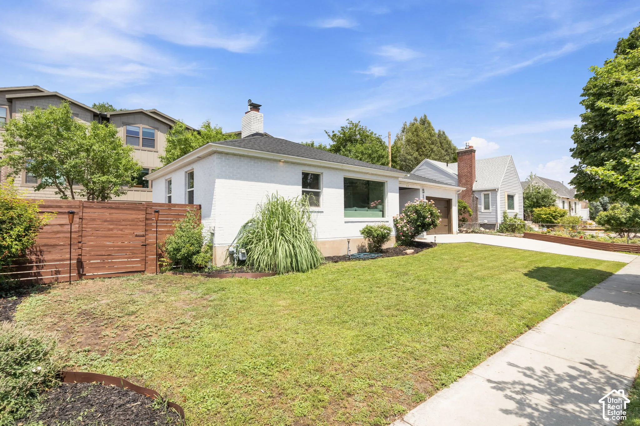 White painted brick exterior featuring a hip roof, chimney, attached garage, and wood-panel privacy fencing