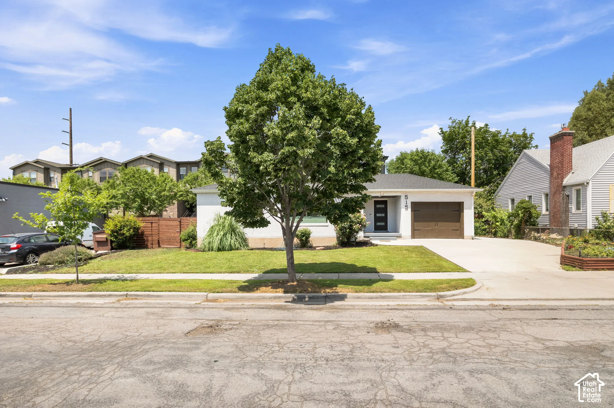 Single-story exterior featuring light-toned siding, an attached garage with a carriage-style door, a concrete driveway, and a front lawn with a mature tree
