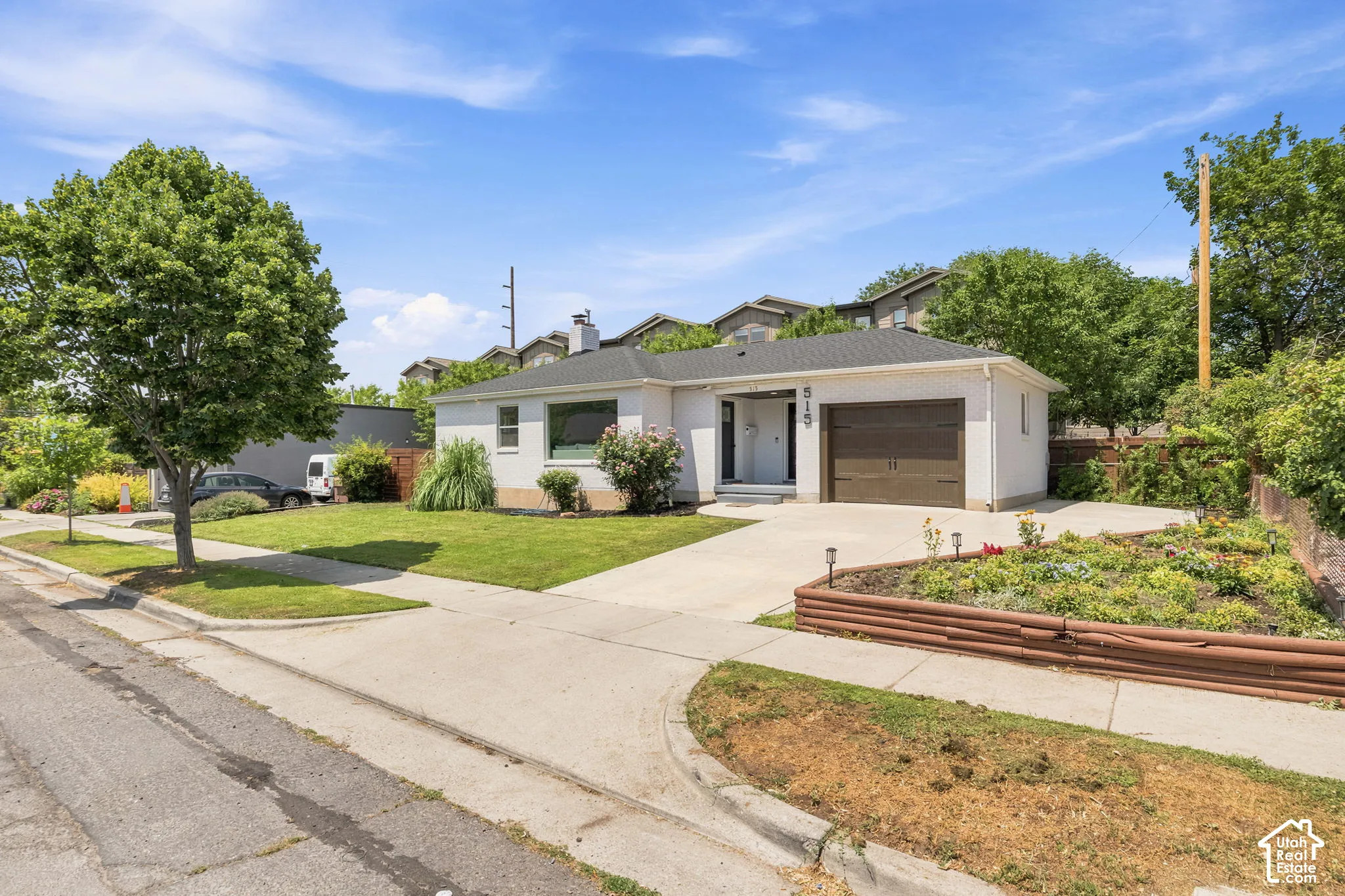 Single-story exterior featuring a painted brick facade, attached one-car garage, concrete driveway, and tiered garden beds