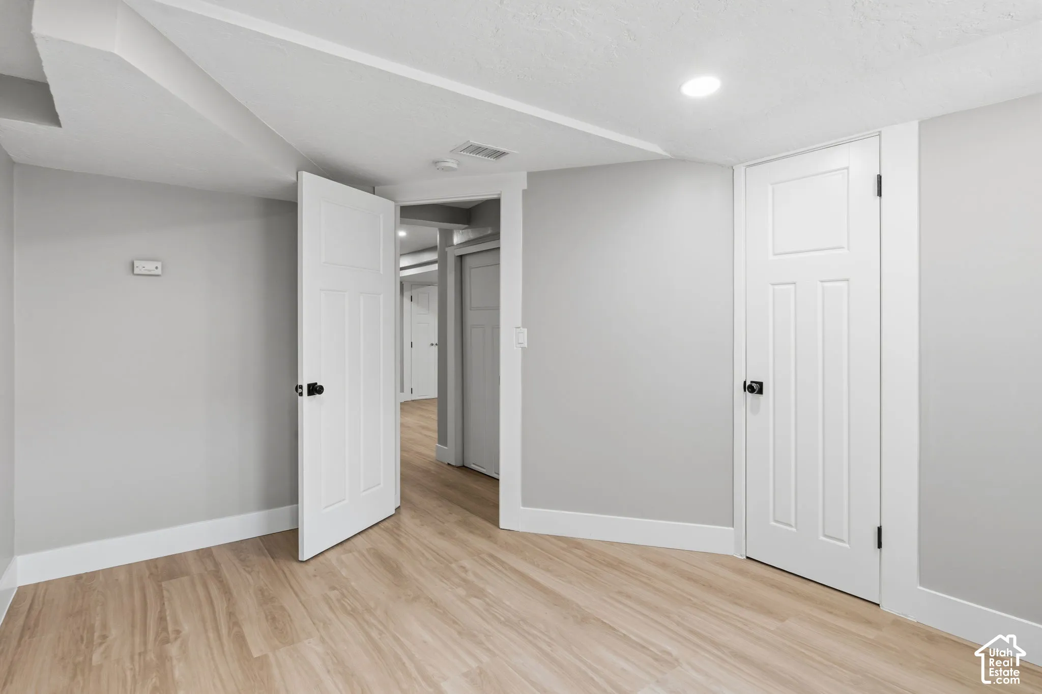 Wood-finish flooring, neutral wall tones, recessed lighting, and white three-panel interior doors with matte black hardware