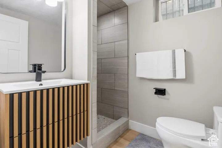Bathroom featuring a wood-slat vanity, rectangular vessel sink with matte black faucet, and a walk-in shower with horizontal grey tile surround