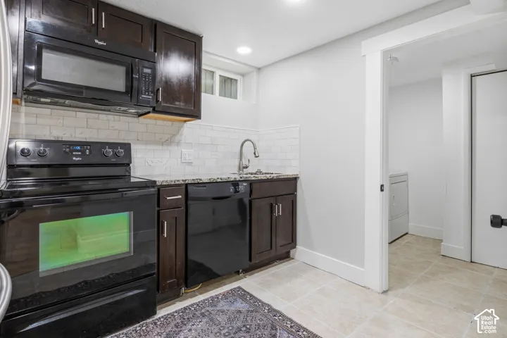 Dark wood cabinetry, speckled stone countertops, subway tile backsplash, integrated black appliances, and tile flooring