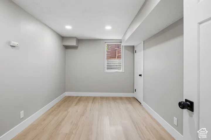 Neutral-toned interior space featuring wood-finish flooring, recessed lighting, a single pane window, and a white interior door with matte black hardware