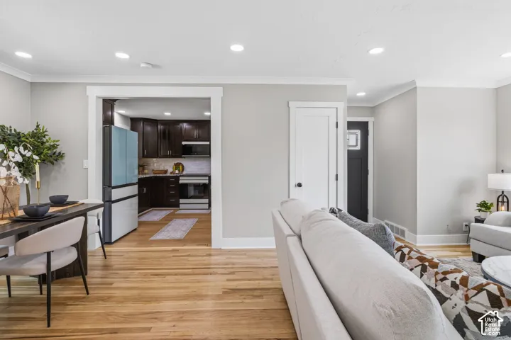 Open-concept interior featuring light wood-finish flooring, recessed lighting, and dark-toned kitchen cabinetry with integrated appliances